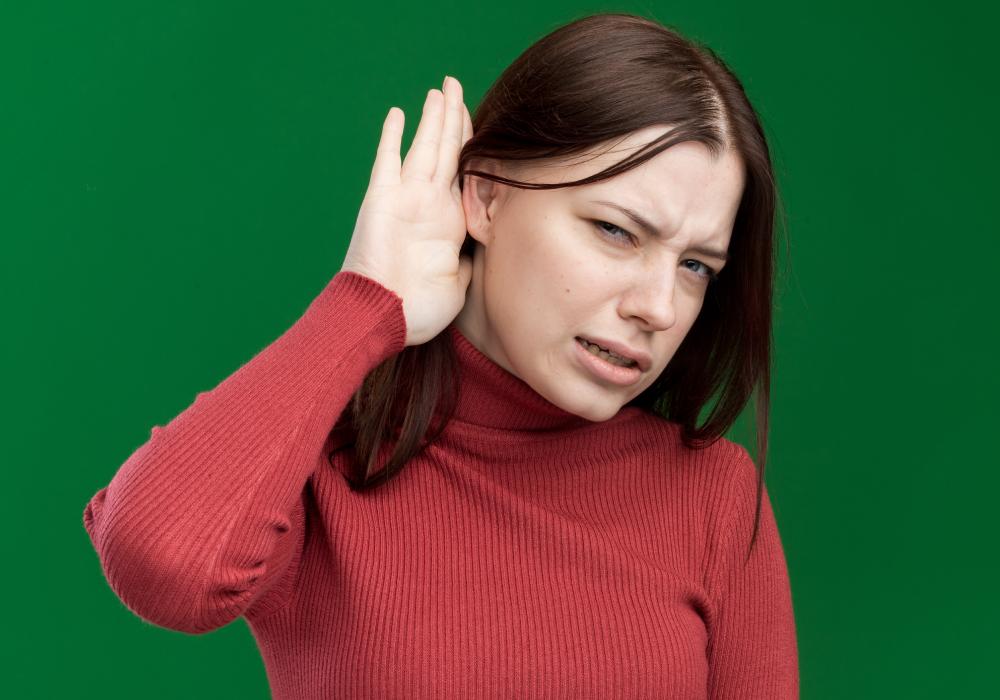 An elderly woman cupping her right hand behind her ear, indicating difficulty in hearing. 