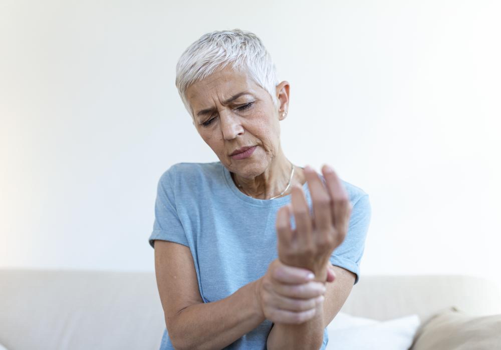 An elderly woman grimacing in pain as she clutches her knee, illustrating the discomfort caused by osteoarthritis.