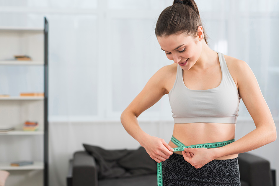 Image of a woman measuring her waist with a tape measure, indicating progress in her weight loss journey.