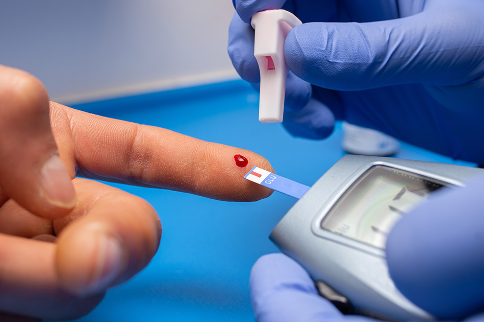 Close-up of a finger with a drop of blood being measured using a glucometer.